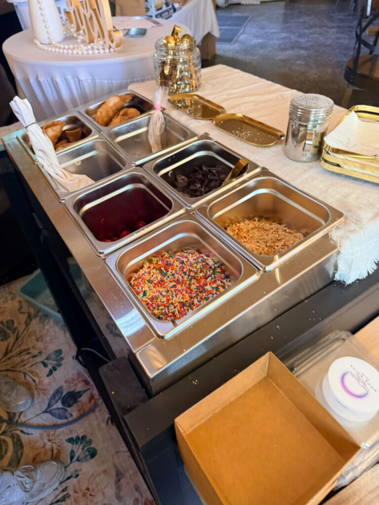 Top-down view of cannoli toppings station with rainbow sprinkles, maraschino cherries, chocolate chips and shells