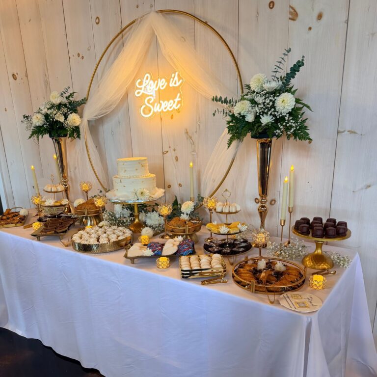 Angled view of a styled wedding dessert table with two-tier cake, macarons and cannoli on gold stands